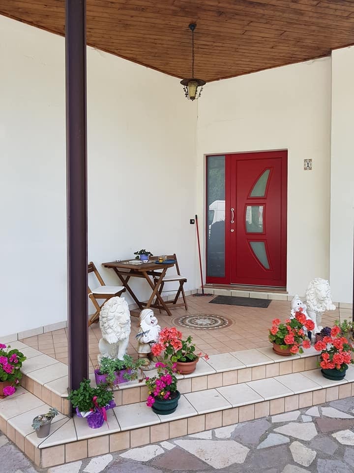 Portico con porta rossa, piante fiorite e tavolino con sedie